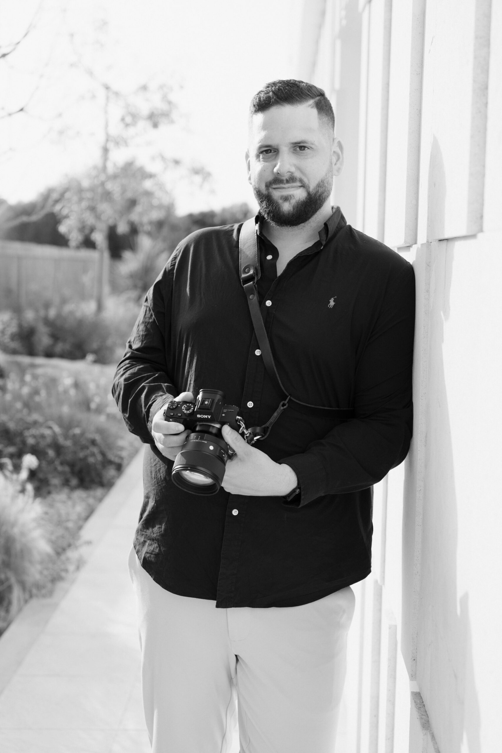 Professioneller Hochzeitsfotograf Hannover mit Kamera lehnt entspannt an Wand im Freien